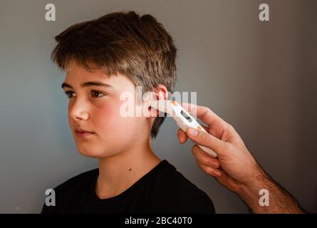 Tween garçon obtenant la température prise avec un thermomètre d'oreille. Banque D'Images