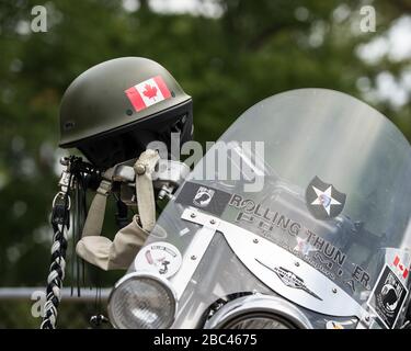 Casque de combat vert avec symbole canadien, accroché sur le guidon d'une moto lors d'un événement d'anciens combattants. Banque D'Images