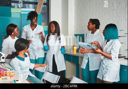 Les étudiantes africaines, les jeunes diplômés ou les médecins discutent du projet en cours. Discussion de groupe expressif énergique dans le centre de recherche. Testi Banque D'Images