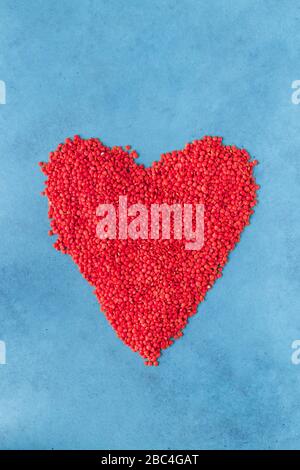 Lentilles rouges éparpillées à la surface sous forme de coeur. Fond bleu Banque D'Images
