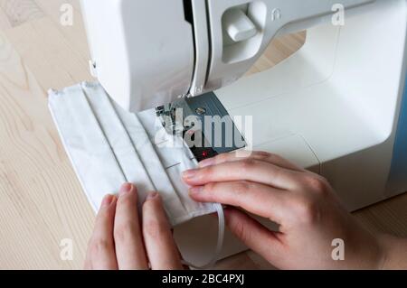 masque à coudre à la maison. Mains féminines, masque avec machine Sew. Protégez-vous contre le coronavirus Banque D'Images