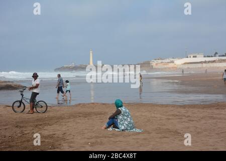 Les habitants de la région se détendent sur la plage publique de Casablanca, au Maroc, avec le phare historique El Hank en arrière-plan. Banque D'Images