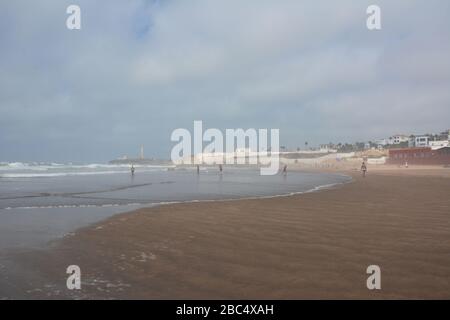 Les habitants de la région se baignent et jouent dans la mer sur la plage publique de Casablanca, au Maroc, avec le phare historique El Hank en arrière-plan. Banque D'Images