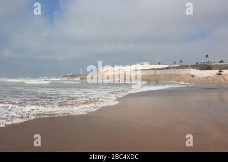 Les habitants de la région prennent les vagues sur la plage publique de Casablanca, au Maroc, avec le phare historique El Hank en arrière-plan. Banque D'Images