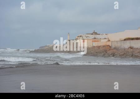 Une photo d'ambiance des vagues qui frappent la plage publique, les murs de mer et le phare historique El Hank à Casablanca, au Maroc. Banque D'Images