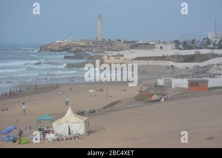 Personnes sur la plage publique de sable à Casablanca, Maroc, avec le phare historique El Hank en arrière-plan. Banque D'Images