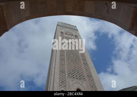 Le plus grand minaret du monde, à 210 m de haut, se trouve à la mosquée Hassan II, Casablanca, au Maroc, que l'on voit ici à travers l'une des arcades de la structure moderne. Banque D'Images