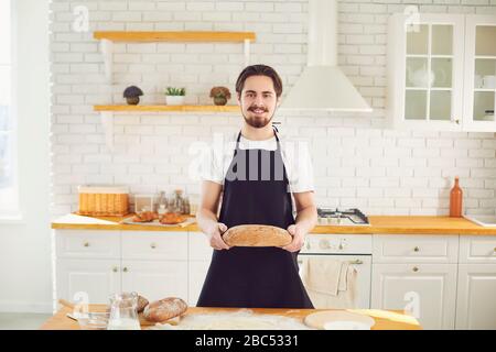 L'homme barbu de Baker tient dans ses mains du pain frais debout à une table dans la cuisine. Banque D'Images