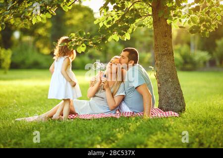 Famille avec bébé sur l'herbe verte dans le parc avec lumière du soleil en été. Le concept d'une famille heureuse. Banque D'Images