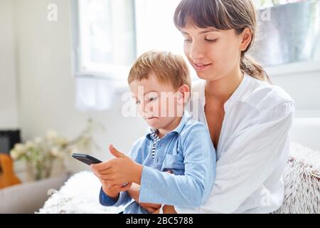 L'enfant joue avec son smartphone sur les genoux de sa mère à la maison Banque D'Images