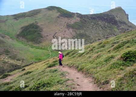 Lone Woman Hiker se descendant jusqu'à la vallée du Shute de Tidna avec le point Sharpnose supérieur en avance sur le sentier côtier du sud-ouest, North Cornwall, Angleterre, Royaume-Uni. Banque D'Images