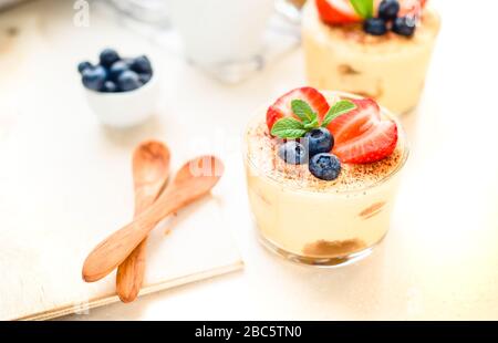 Tiramisu dessert exquis, faits maison dans les verres décorés de fraise, de bleuet, de menthe sur la table en bois blanc, Banque D'Images