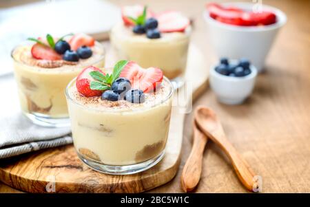 Tiramisu dessert exquis, faits maison dans les verres décorés de fraise, de bleuet, de menthe sur la table en bois blanc, Banque D'Images