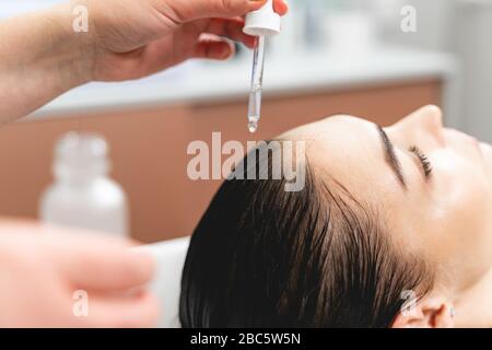 Gros plan sur la main féminine qui goutte de sérum sur les cheveux Banque D'Images