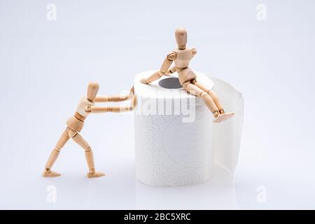 Les personnes en bois travaillant avec un papier blanc de rouleau de toilette isolé devant un fond blanc, l'une d'elles est assise sur le rouleau tandis que l'autre le pousse Banque D'Images
