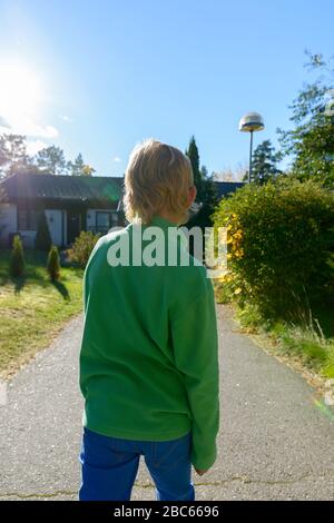 Vue arrière d'un jeune garçon avec des cheveux blonds dans la cour avant Banque D'Images