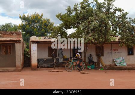 LILONGWE, MALAWI, AFRIQUE - 1er AVRIL 2018: Les Africains sont assis à la maison, s'exprimant avec une femme sur le bycicle le long de la route où le chien a le repos Banque D'Images