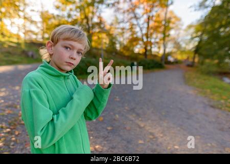 Jeune beau garçon avec signe de paix au parc en automne Banque D'Images