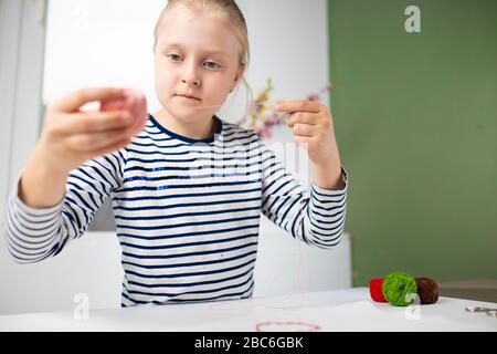 Jolie fille faisant des travaux ménagers pendant la quarantaine, broderie avec des fils de couleur 1 Banque D'Images