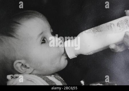 Belle photographie noir et blanc vintage des années 1970 d'une jeune fille caucasienne belle boire du lait à partir d'une bouteille Banque D'Images