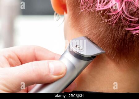 Main de coiffeur rase femme cheveux rose avec rasoir électrique vue arrière dans le salon de beauté gros plan. Banque D'Images