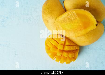 Quatre fruits de mangue entiers sur une table bleu vif et coupés en tranches. Gros fruits jaunes juteux Banque D'Images