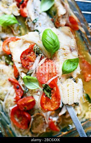 Poisson blanc (pollock, morue, merlu) cuit avec tomates, herbes italiennes et feuilles de basilic frais dans leur propre jus. Délicieux fruits de mer méditerranéens Banque D'Images