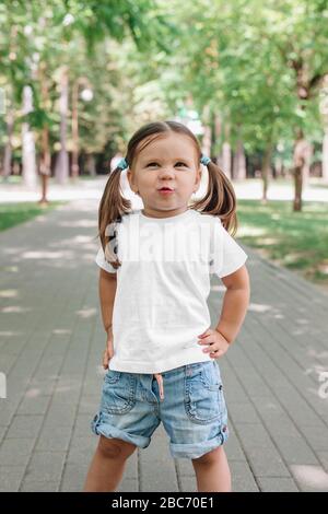 petite fille souriante dans un t-shirt blanc vierge debout dans le parc Banque D'Images