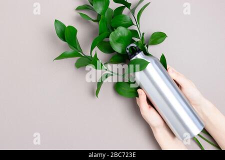 Les mains tiennent la bouteille en métal. Concept zéro déchet avec bouquer de feuilles vertes sur fond gris. Banque D'Images