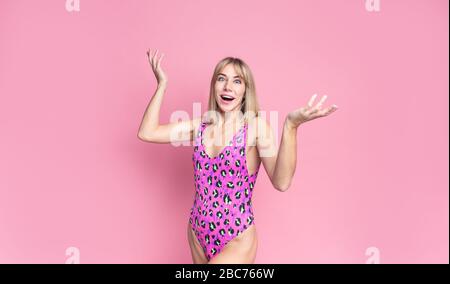 Surprise superbe femme blonde dans un maillot de bain rose léopard avec une large bouche ouverte regardant l'appareil photo, souriant sur un fond rose Banque D'Images