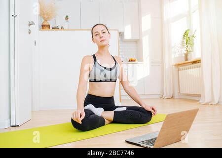 Femme fatiguée faisant du yoga à la maison, assis dans une posture de lotus, regardant la caméra Banque D'Images