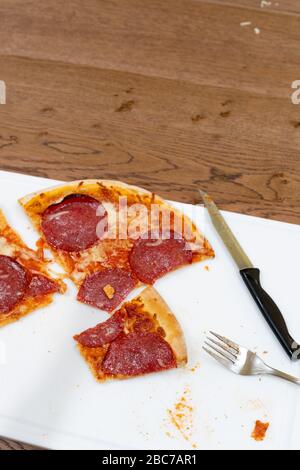 Une pizza salami est coupée en tranches lors d'un repas sur un tableau blanc. Banque D'Images