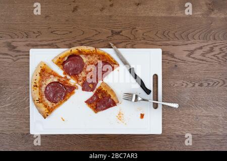 Une pizza salami est coupée en tranches lors d'un repas sur un tableau blanc. Banque D'Images