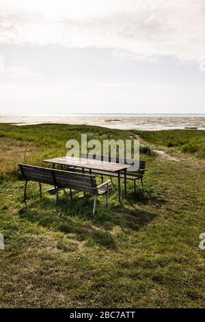 Table de pique-nique avec deux bancs en bois sur un pré vert avec vue sur la mer des Wadden au soleil. Banque D'Images