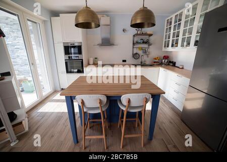 Cuisine blanche et lumineuse avec îlot bleu et deux lampes suspendues en laiton. Vue centrale. Banque D'Images