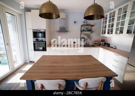 Cuisine blanche et lumineuse avec îlot bleu et deux lampes suspendues en laiton. Vue centrale avec îlot de cuisine au premier plan. Banque D'Images