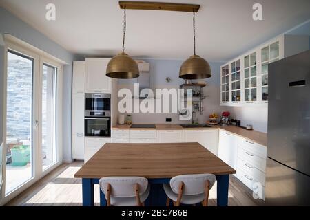 Cuisine blanche et lumineuse avec îlot bleu et deux lampes suspendues en laiton. Vue centrale. Banque D'Images