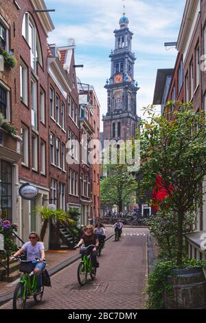 Visites touristiques sur les vélos à vélo dans une rue étroite surplombant la tour de l'église de Westerkerk à Amsterdam, Pays-Bas Banque D'Images