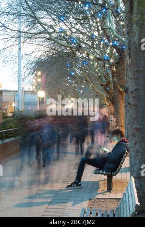 Adolescent garçon Sat sur banc sur smartphone sur South Bank London Banque D'Images