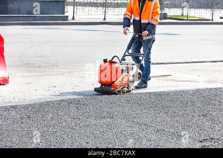 L'entretien sur route des travailleurs utilise un compacteur à plaque vibrante qui compacte l'asphalte sur le site de réparation sur route. Banque D'Images