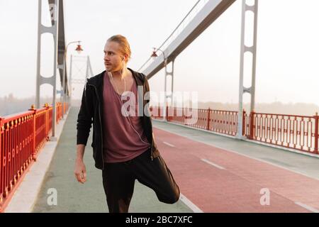 Un jeune sportif séduisant qui travaille sur un pont, fait des exercices d'étirement Banque D'Images