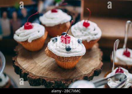 Cupcakes avec cherrie et bleuets sur support en bois, foyer sélectif Banque D'Images