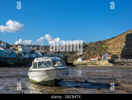 Un petit bateau blanc s'est engrange dans le port de Staithes lors d'une journée ensoleillée avec des skys bleus. Banque D'Images