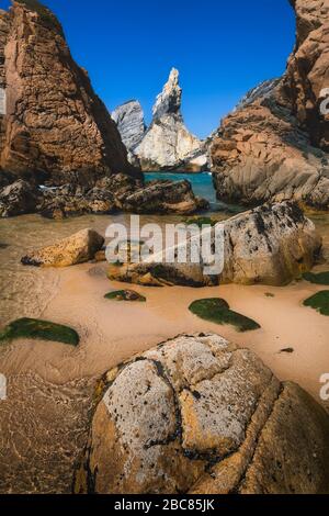 Plage d'Ursa, Sintra, Portugal. Paysage marin épique avec falaises abruptes qui s'élèvent des eaux turquoise de la mer. Belle plage de sable doré intacte avec grand sto Banque D'Images