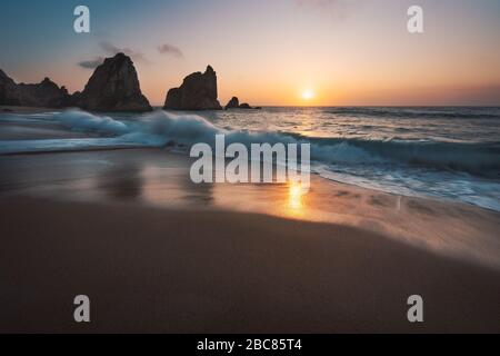 Portugal Plage d'Ursa sur la côte atlantique. Reflet du coucher du soleil. La vague blanche se dirige vers la plage de sable avec une silhouette de roche en arrière-plan. Paysagiste pittoresque Banque D'Images