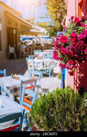 Taverne traditionnelle grecque aux couleurs vives avec des fleurs violettes dans l'étroite rue méditerranéenne le jour chaud de l'été. Banque D'Images