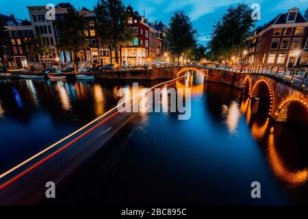 Soirée d'Amsterdam illuminée en ville. Des sentiers de lumière pour bateaux touristiques et des réflexions de ponts sur les canaux Leidsegracht et Keizersgracht. Ex long Banque D'Images