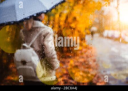 Silhouette de fille porter une veste d'aviateur avec un parapluie derrière la fenêtre couverte de gouttes de pluie en automne doré. Coucher de soleil rétroéclairé Banque D'Images