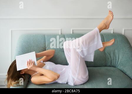 femme dans la maison vêtements rester à la maison et lire un livre tout en couché sur un canapé. fille reposant à la maison et se reposant autour de vous Banque D'Images