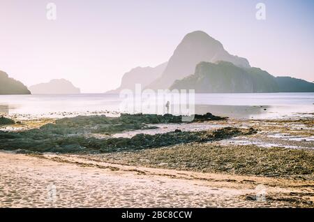 Photographe solitaire au-dessus des rochers lors de la basse marée photo le matin lever du soleil lumière devant l'incroyable île Cadlao, El-Nido, Palawan, Phi Banque D'Images